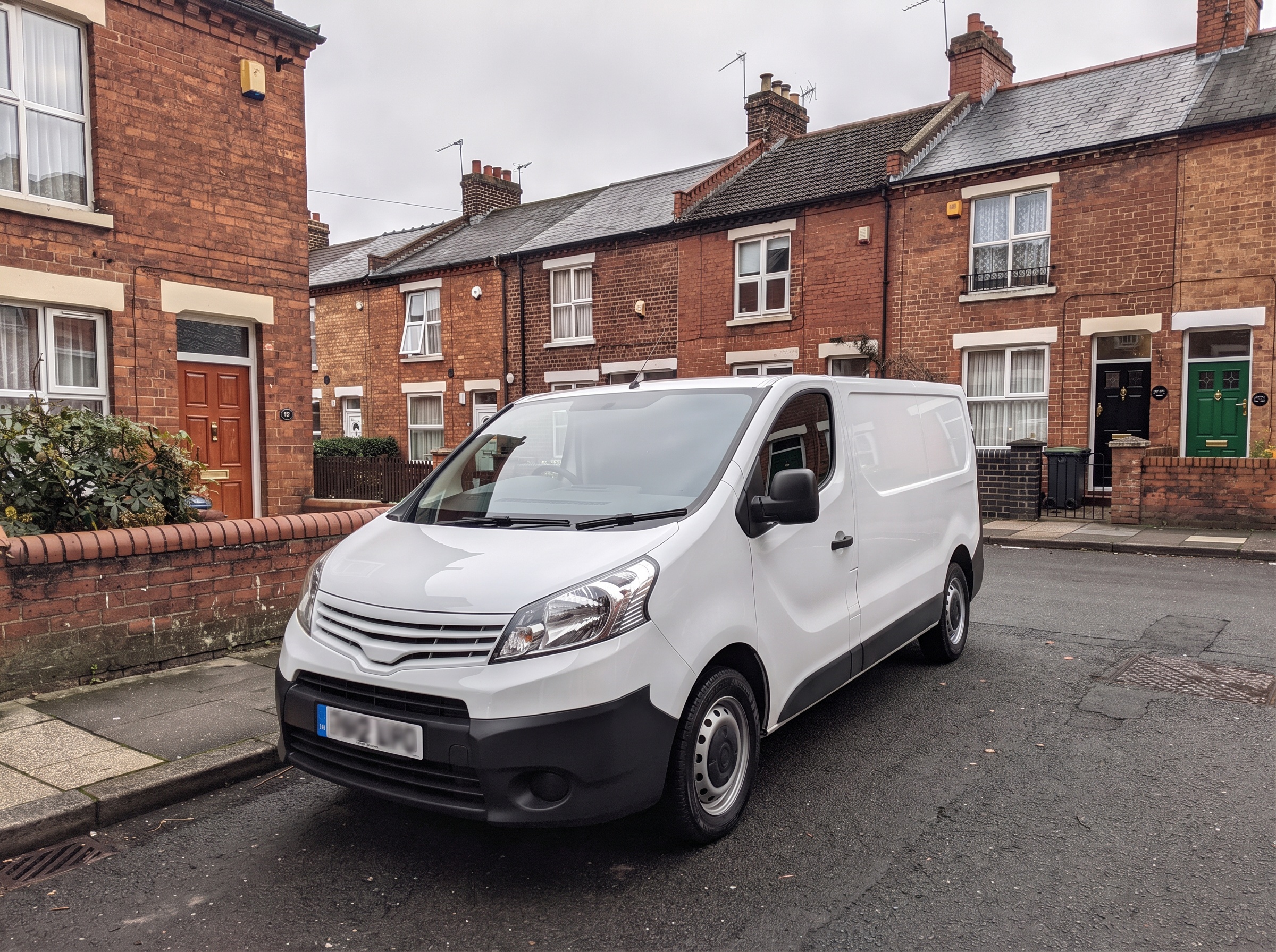 A clean white van parked on a terraced street of red brick houses